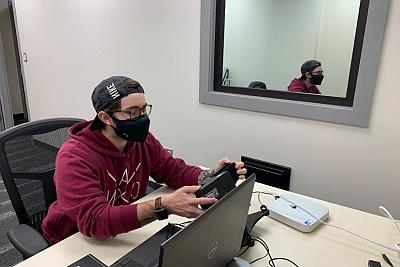 一名学生拿着眼球追踪设备坐在电脑桌前